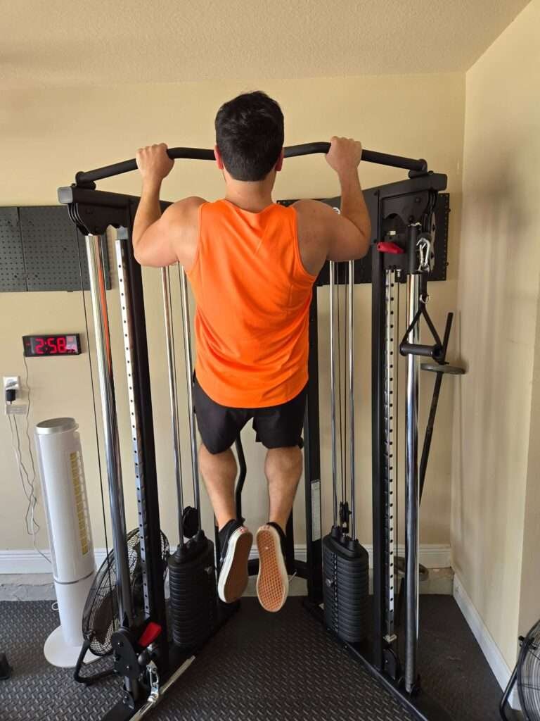 Man performing a pull-up on a cable machine in a home gym setting.