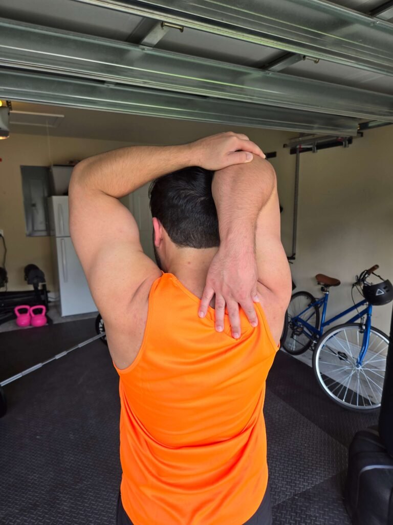 Man performing a triceps stretch in a home gym environment.