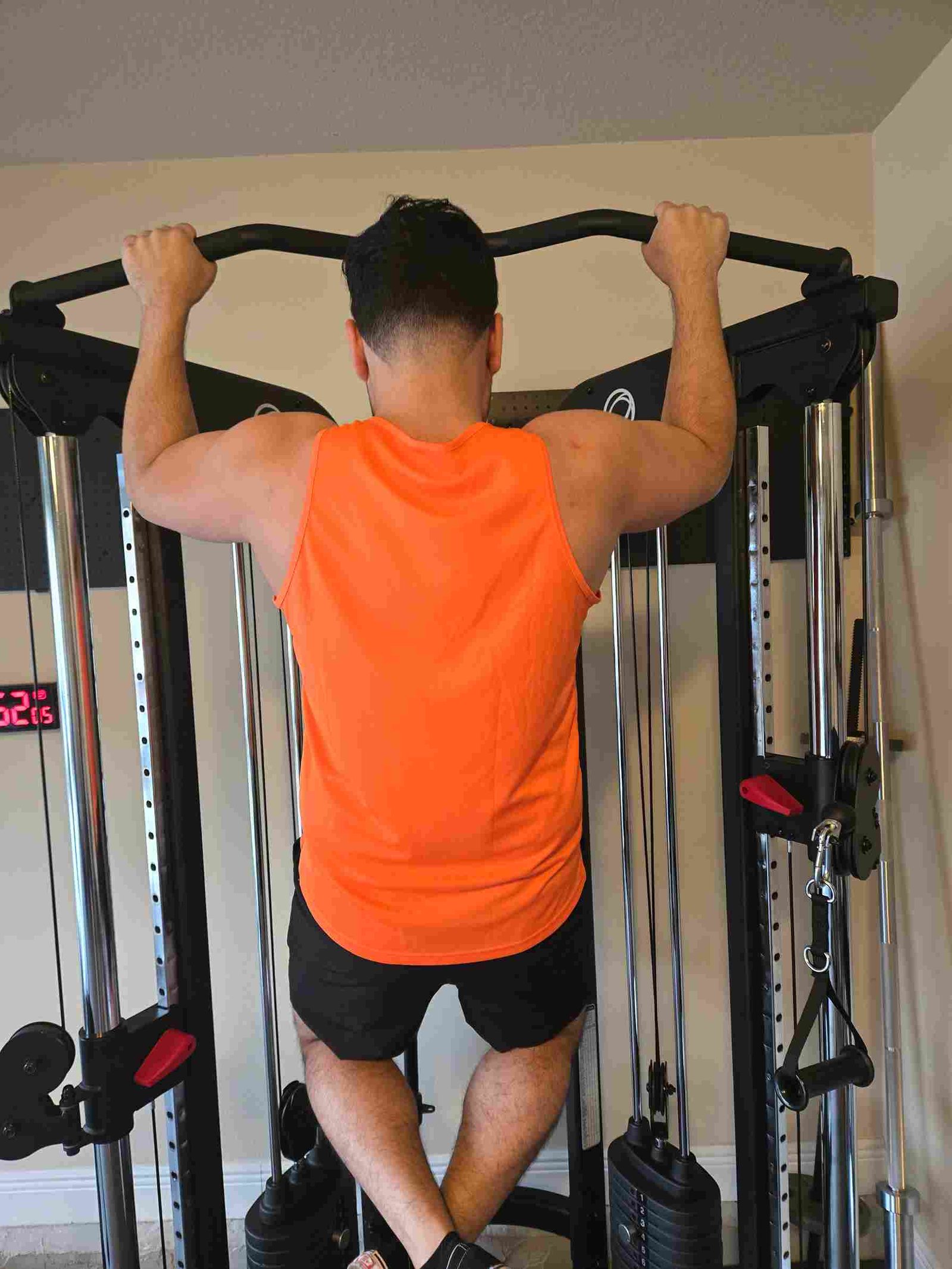 Bodyweight Pull-Up in Home Gym A man performing a bodyweight pull-up in a home gym, wearing an orange tank top and black shorts.