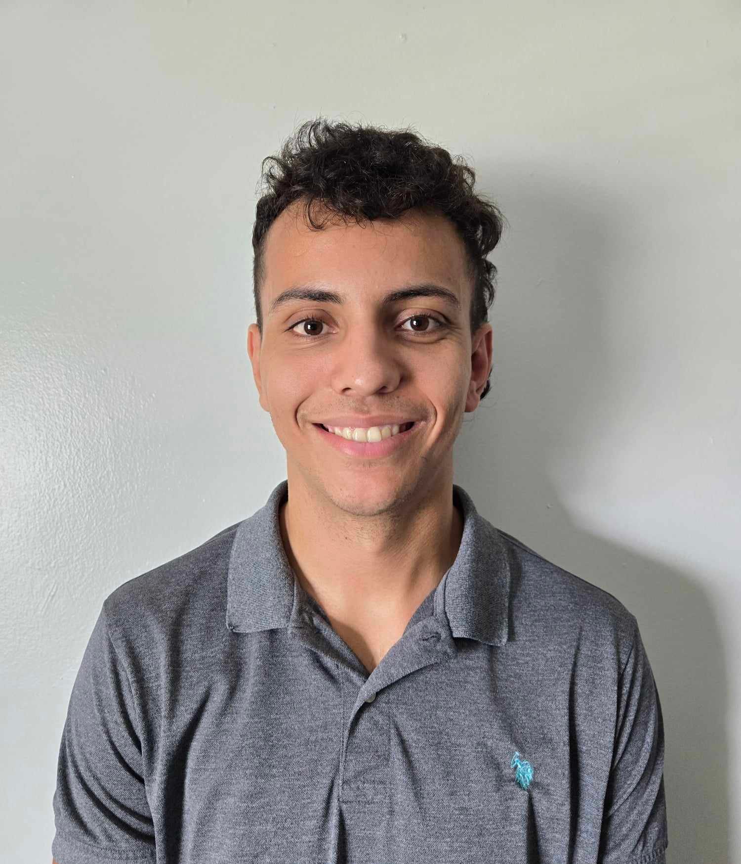 Chris Geliga – Certified Personal Trainer Headshot Chris Geliga smiling in a gray polo shirt against a light wall background.